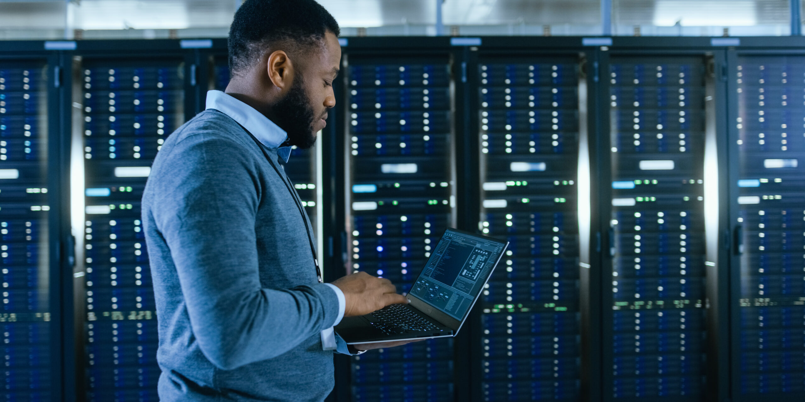 An IT professional conducting a security audit in a server room with a laptop.
