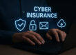 Hands typing on a laptop with glowing cybersecurity icons and the words “Cyber Insurance,” symbolizing digital protection for small businesses.