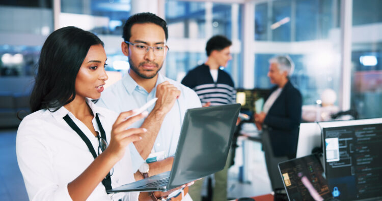 IT professionals collaborating in a modern office environment, reviewing information on a laptop as part of a co-managed IT support strategy.