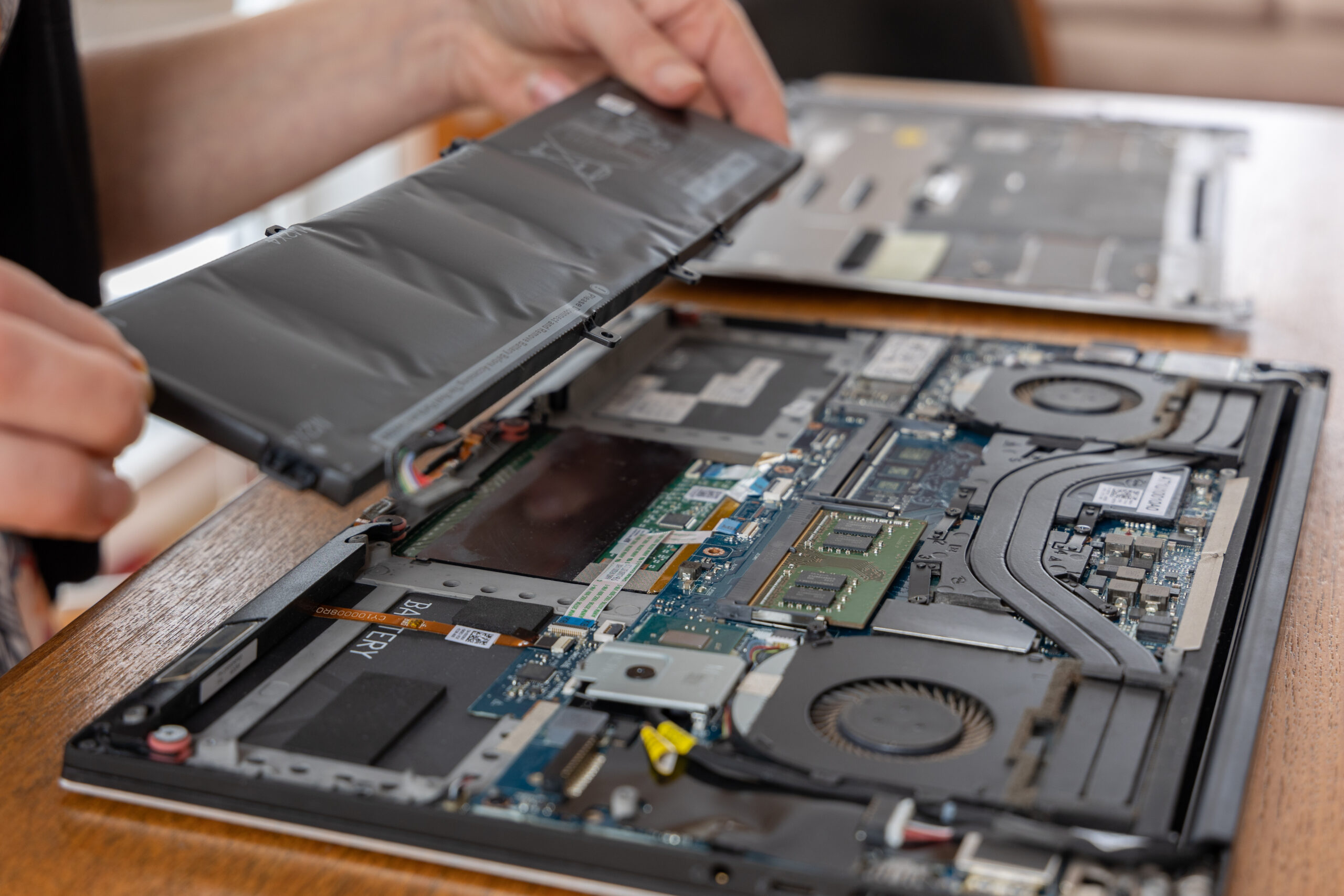 Technician removing a laptop battery during internal hardware inspection, showing signs of wear and components that may need replacement in a business refresh cycle.