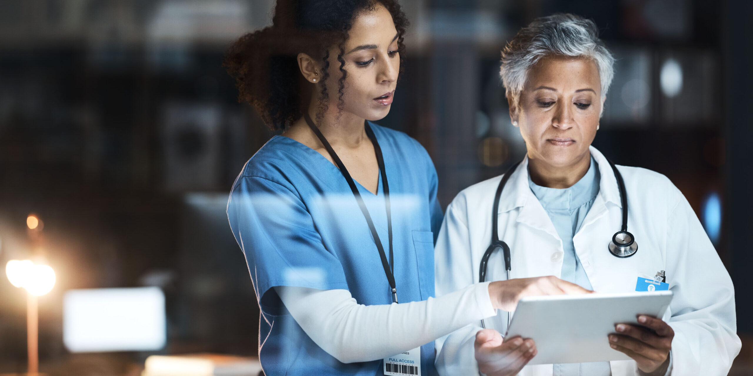 Two healthcare professionals reviewing patient information on a tablet, demonstrating the use of healthcare technology and electronic health records in a clinical environment.