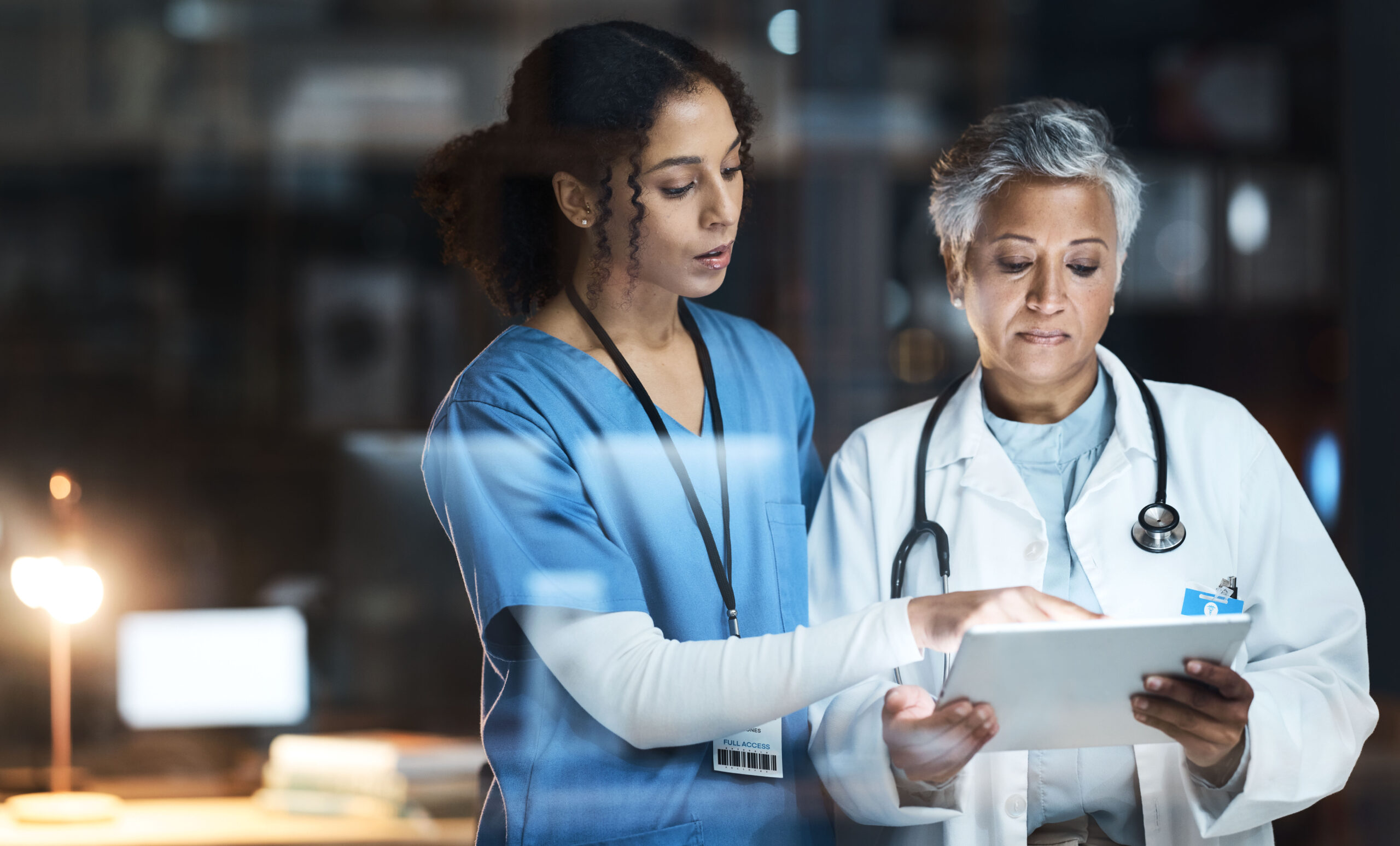 Two healthcare professionals reviewing patient information on a tablet, demonstrating the use of healthcare technology and electronic health records in a clinical environment.