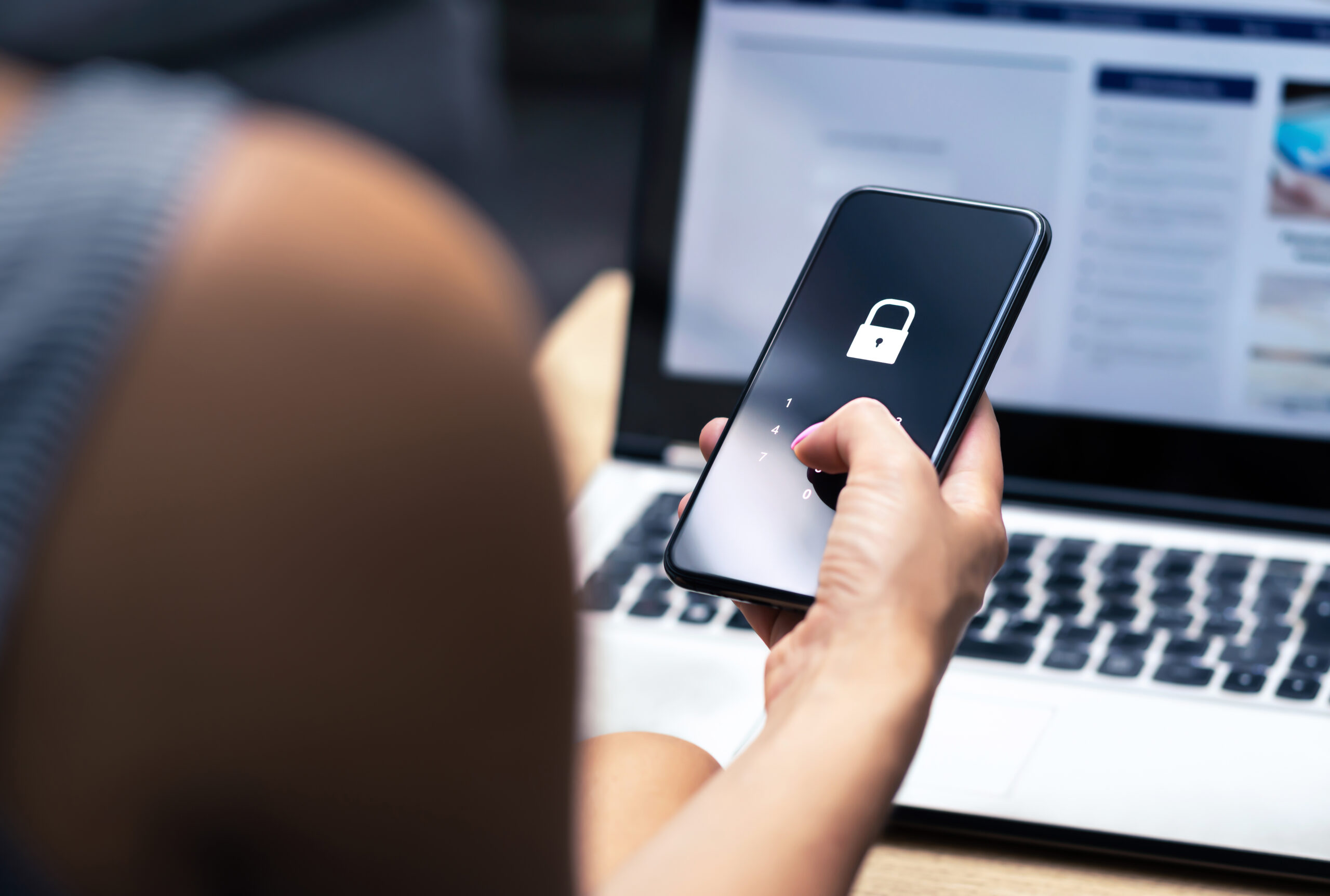 User entering a passcode on a smartphone in front of a laptop, representing real-time threat detection and response in a SIEM and SOC environment.