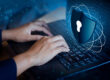 Person typing on a laptop with a digital cybersecurity shield overlay representing security hardening, access control, and protection against cyber threats.