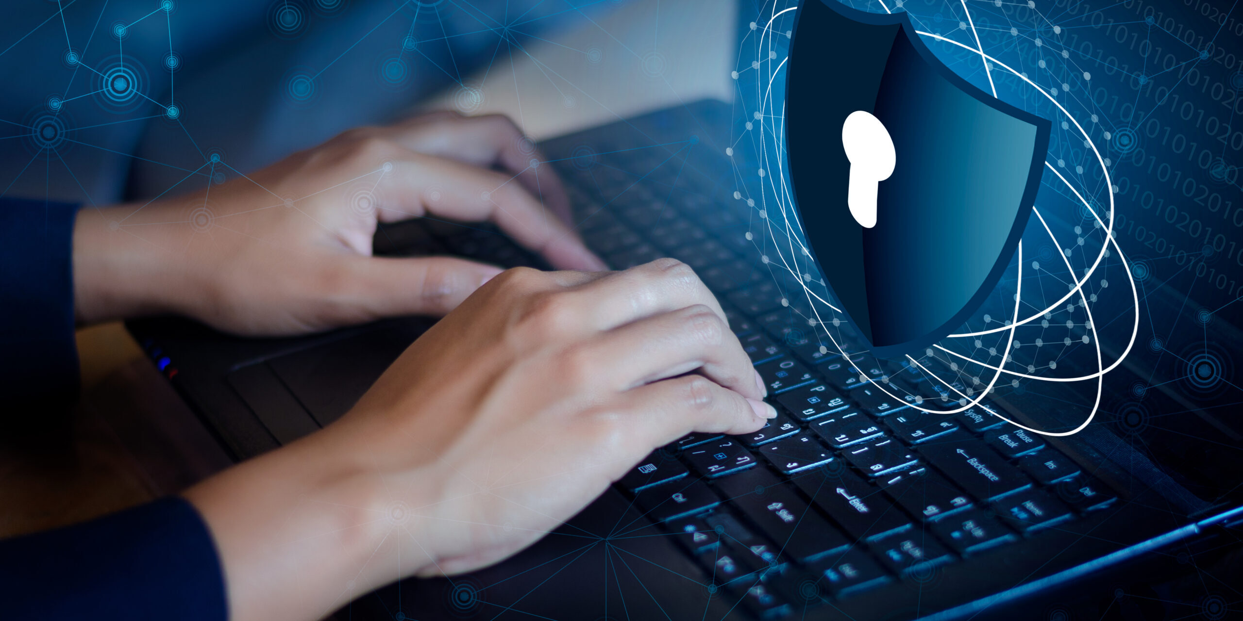 Security Hardening Strategies for Protecting Business Systems Person typing on a laptop with a digital cybersecurity shield overlay representing security hardening, access control, and protection against cyber threats.