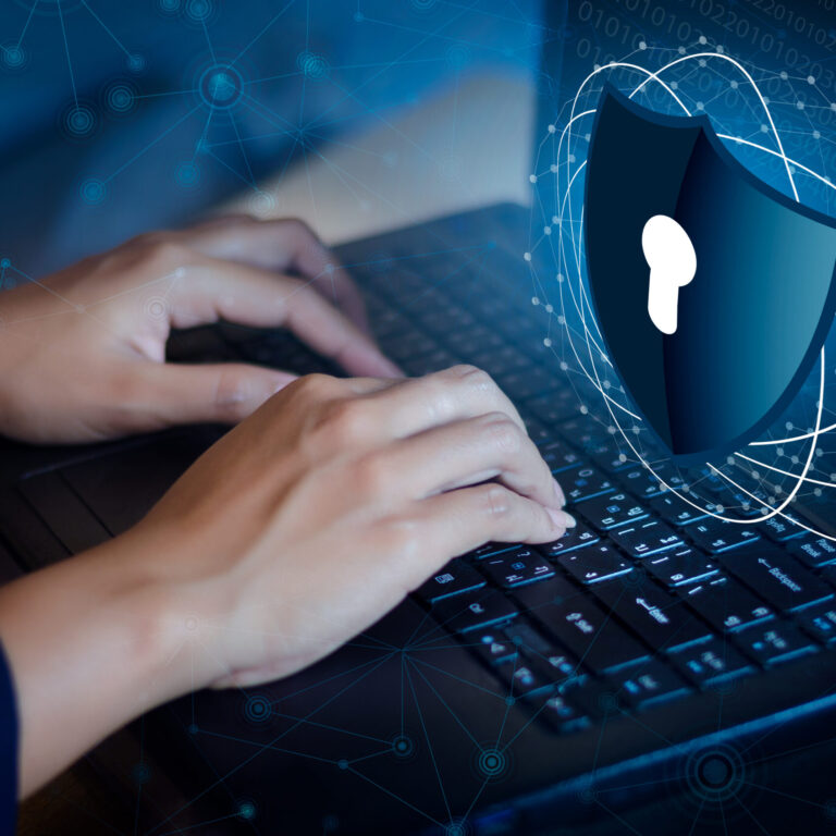Person typing on a laptop with a digital cybersecurity shield overlay representing security hardening, access control, and protection against cyber threats.