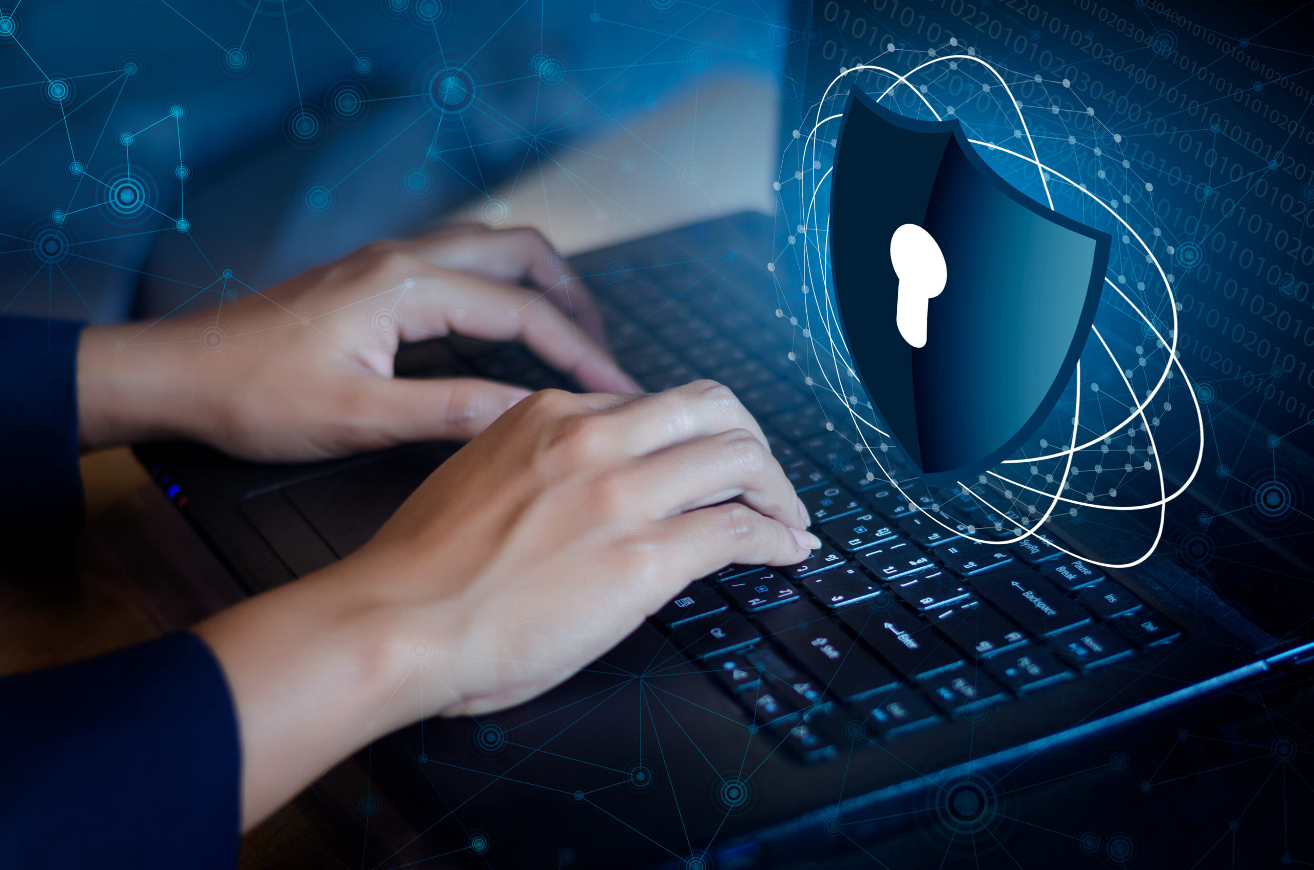 Person typing on a laptop with a digital cybersecurity shield overlay representing security hardening, access control, and protection against cyber threats.