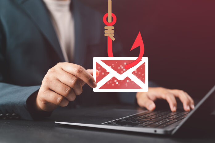 Business professional holding a phishing email icon over a laptop, illustrating email spoofing attacks and domain protection through email authentication protocols.