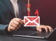 Business professional holding a phishing email icon over a laptop, illustrating email spoofing attacks and domain protection through email authentication protocols.