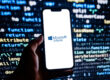 A smartphone displaying the Microsoft Intune logo against a blurred background of computer code, representing cloud-based endpoint management, mobile device security, and Microsoft 365 device administration.