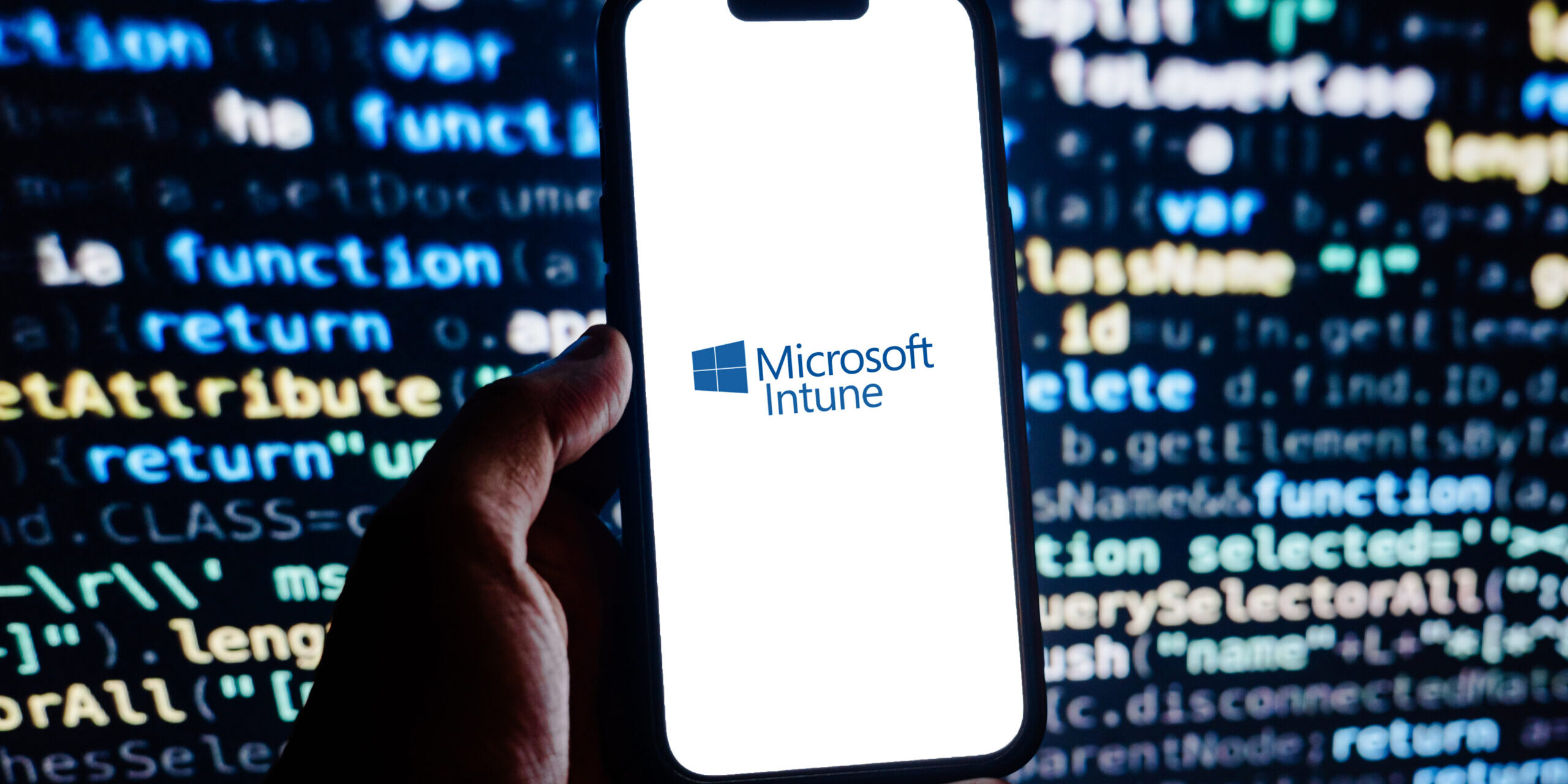 Microsoft Intune Helps Businesses Secure and Manage Devices A smartphone displaying the Microsoft Intune logo against a blurred background of computer code, representing cloud-based endpoint management, mobile device security, and Microsoft 365 device administration.